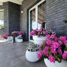 three large white planters filled with pink flowers on a porch next to a brick building