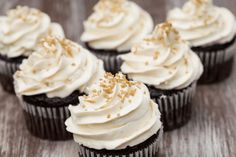 cupcakes with white frosting and sprinkles on wooden table top