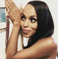 a woman leaning against a wall with her hands on her head and looking at the camera