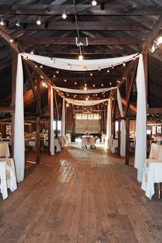 the inside of a barn with tables and chairs set up for a wedding reception in white linens