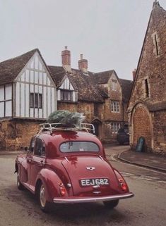 an old red car with a christmas tree on the roof parked in front of some buildings