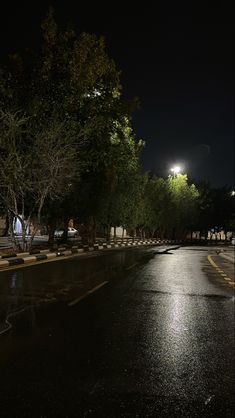 an empty street at night with people walking on the sidewalk and trees in the background