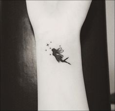 a black and white photo of a small wrist tattoo with a tiny fairy on it