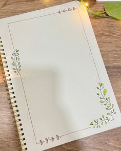 an open notebook on top of a wooden table next to a pen and flower pot