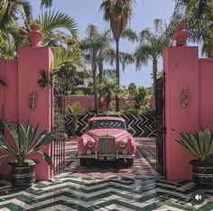 an old pink car is parked in front of a gated driveway with potted plants