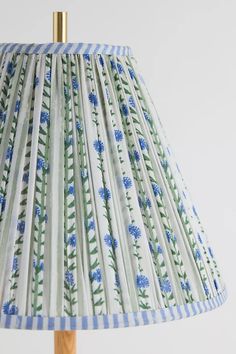 a lamp shade with blue flowers on white and green striped lampshade against a white wall