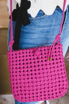 a woman holding a pink crocheted purse with a black bow on it's shoulder