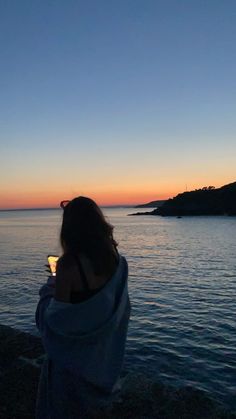 a woman standing on top of a beach next to the ocean holding a cell phone