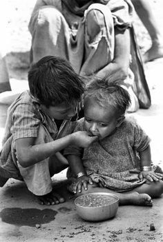 two small children sitting on the ground with their hands over each other's mouths