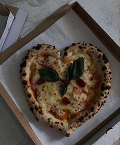 a heart shaped pizza in a box with basil leaves on the top and pepperoni