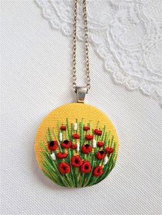 a necklace with red and white flowers painted on the front, sitting on a lace doily