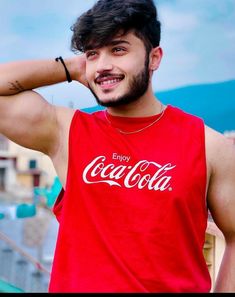 a man wearing a red coca cola tank top with his hand on his head and looking at the camera