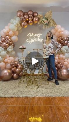 a woman standing in front of a table with balloons on it and a happy birthday sign