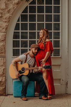 a man holding a guitar next to a woman in a red dress on a bench