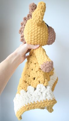 a hand holding a crocheted giraffe hanging from a hook on a wall