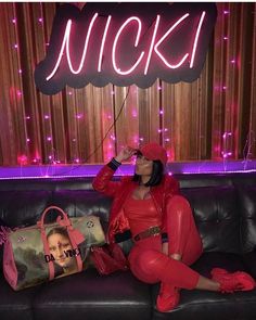 a woman sitting on top of a couch in front of a neon sign that reads nicki