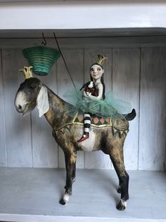 a statue of a girl riding on top of a horse with a green lantern hanging from it's back