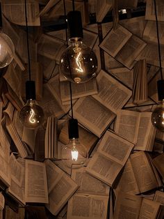 several light bulbs are hanging from the ceiling made out of books and lit by lamps