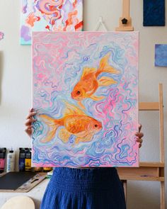 a woman holding up a painting with two goldfishs in the water on it