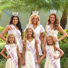 four women in white dresses and tiaras posing for the camera with one woman wearing a crown