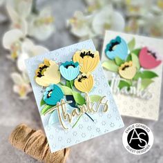 two greeting cards with flowers and the words thank you on them, sitting next to twine of twine spools