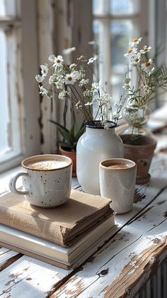 two coffee mugs sitting on top of a book next to a vase with flowers