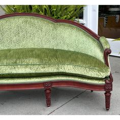 a green couch sitting on top of a sidewalk next to a potted fern plant