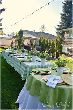 a table set up with green and white checkered cloths, plates and flowers