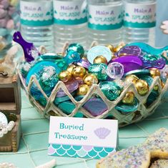 there is a bowl full of candies and cookies on the table with water bottles in the background