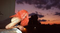 a woman with red hair is leaning on a ledge at night in front of the city skyline