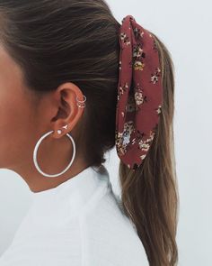 a woman with her hair in a ponytail wearing large hoop earrings and a flowered headband