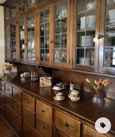 an old fashioned wooden cabinet with glass doors and dishes on the top shelf in a kitchen