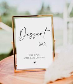 a dessert bar sign sitting on top of a wooden table next to a white feather