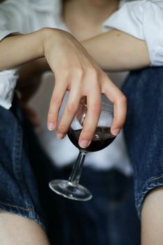 a person sitting down holding a wine glass with their hand on the top of it