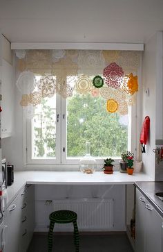 a small kitchen with white cabinets and colorful curtains on the window sill over the sink