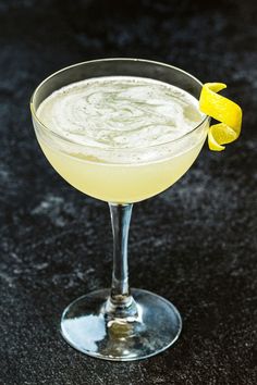 a glass filled with a drink sitting on top of a black counter next to a lemon wedge