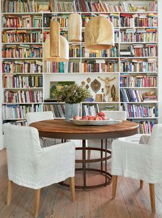 a dining room table surrounded by bookshelves with chairs around it and a bowl of fruit on the table