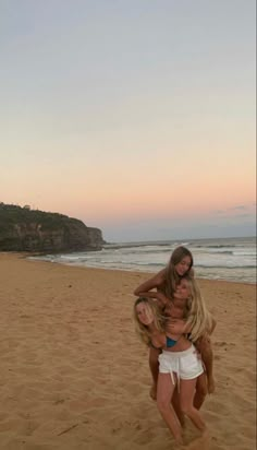 two women are standing on the beach with their arms around each other as they hug