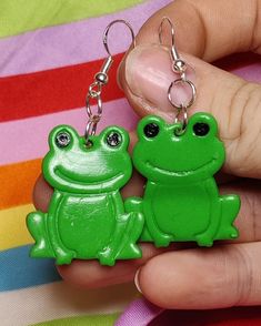 two green frog keychains are being held by someone's hand on a colorful blanket