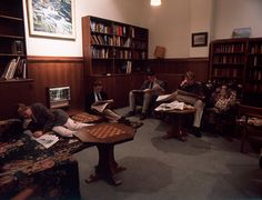 four people are sitting in a library with books on the tables and one person is playing chess