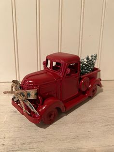 an old red truck with a christmas tree in the back is sitting on a table