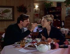 a man and woman sitting at a table with food in front of them, eating