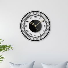 a white and black clock on the wall in a living room with couches, pillows and potted plant