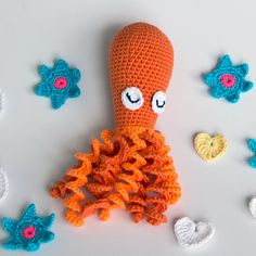 an orange crocheted octopus with eyes and arms surrounded by other crocheted items