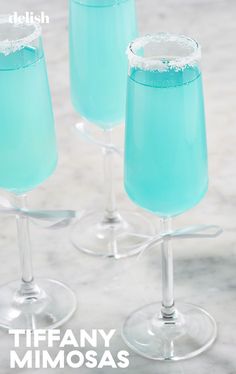 three glasses filled with blue liquid on top of a marble counter topped with ice and sprinkles