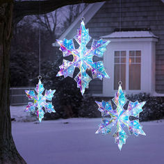 three snowflakes hanging from a tree in front of a house