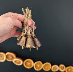 a hand is holding three bells in front of an orange slice garland with twine