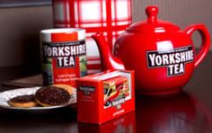 tea and cookies on a table next to a red teapot with yorkshire tea in it