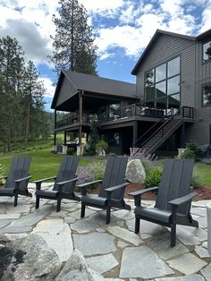 several lawn chairs sitting in front of a large house with a stone patio and steps leading up to it