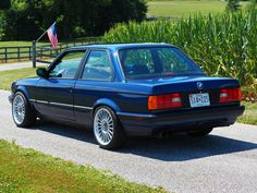 a blue car parked on the side of a road next to a corn field and an american flag